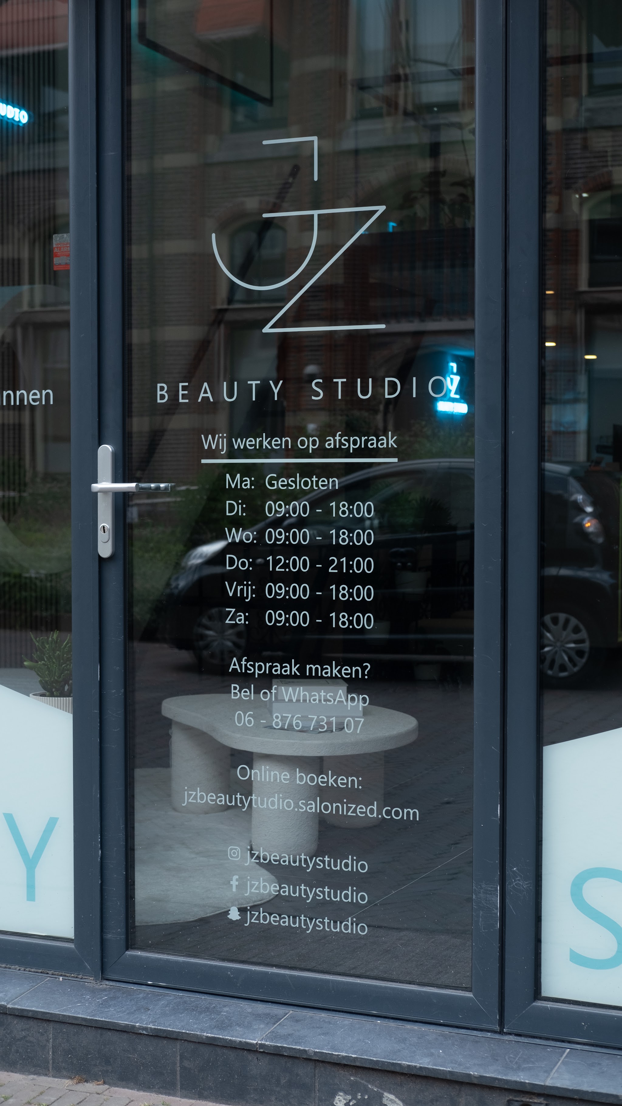 De deur van de studio met het logo, de openingstijden en Wij werken op afspraak
